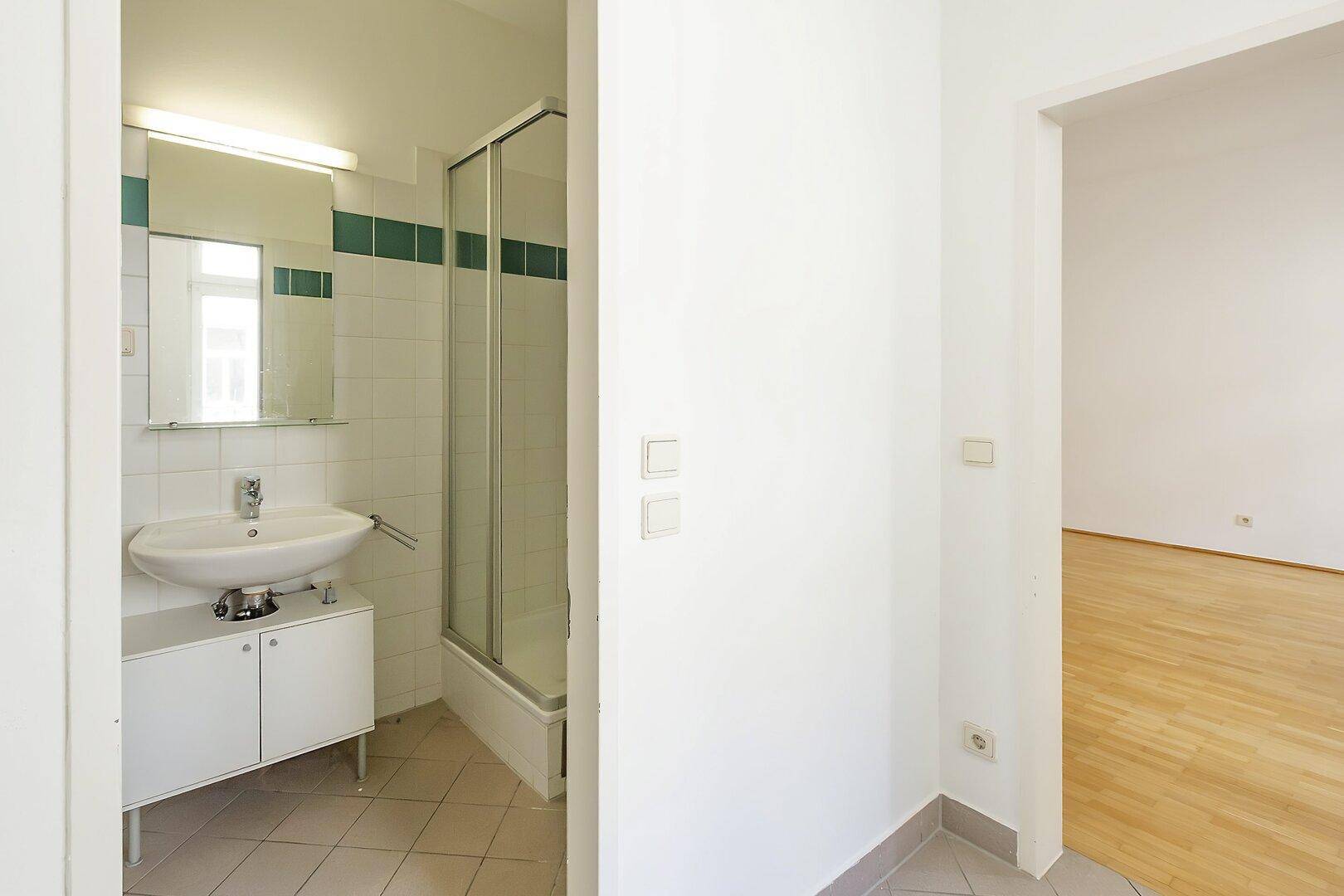 Flur mit Zugang zu einem Badezimmer mit Dusche und einem weiteren Zimmer.