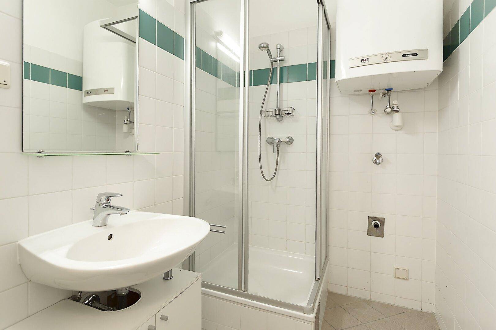 Kleines Badezimmer mit Dusche, Waschbecken und weiß-grünen Fliesen.