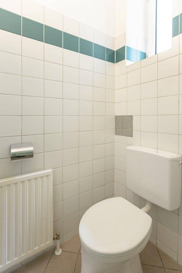 Separate Toilette mit Heizkörper und weiß-grünen Wandfliesen.