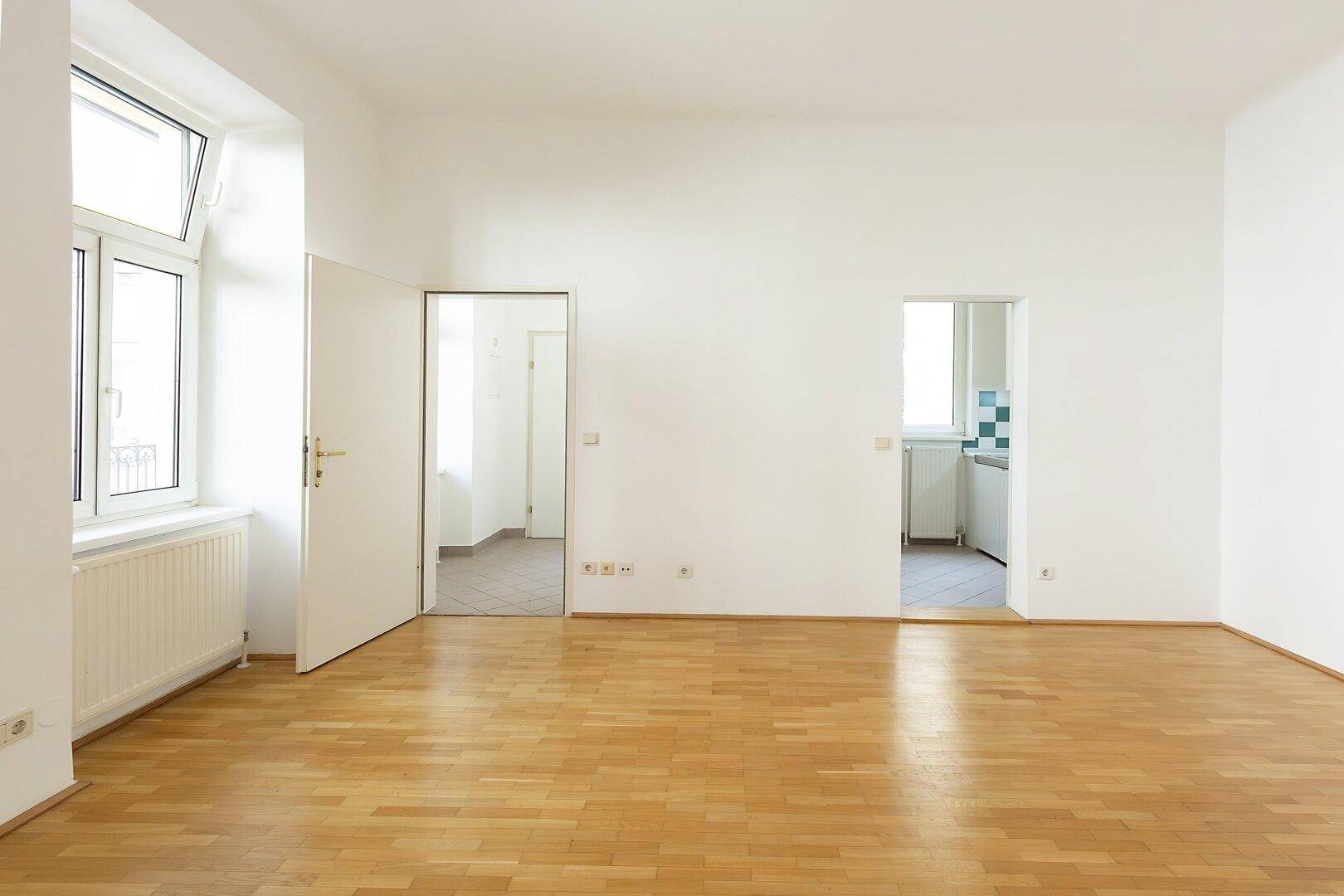 Geräumiges, helles Zimmer mit Parkettboden und mehreren Türen zu angrenzenden Räumen.