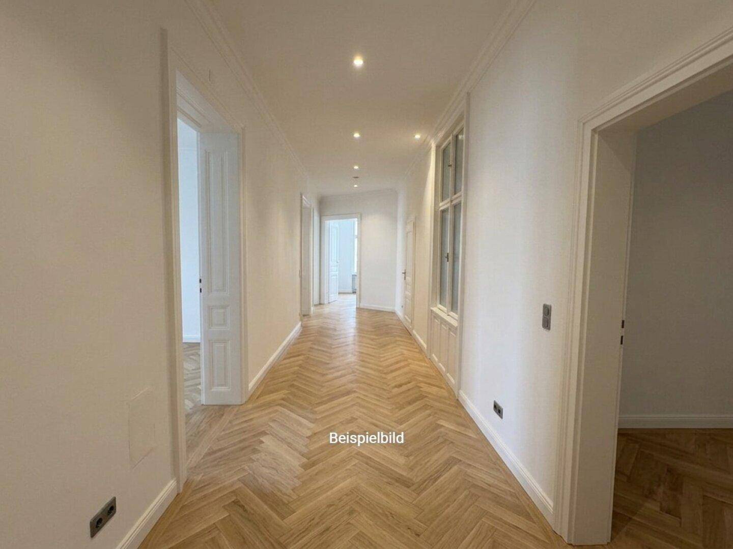 Langer, heller Flur mit Fischgrätparkett und hohen Decken, der zu weiteren Räumen führt.