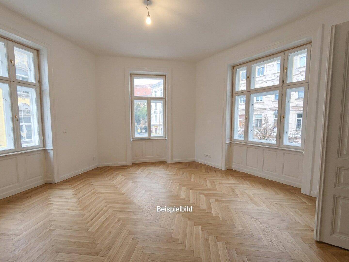 Helles Zimmer mit Fischgrätparkett, hohen Decken und großen Fenstern mit Blick auf die Straße.