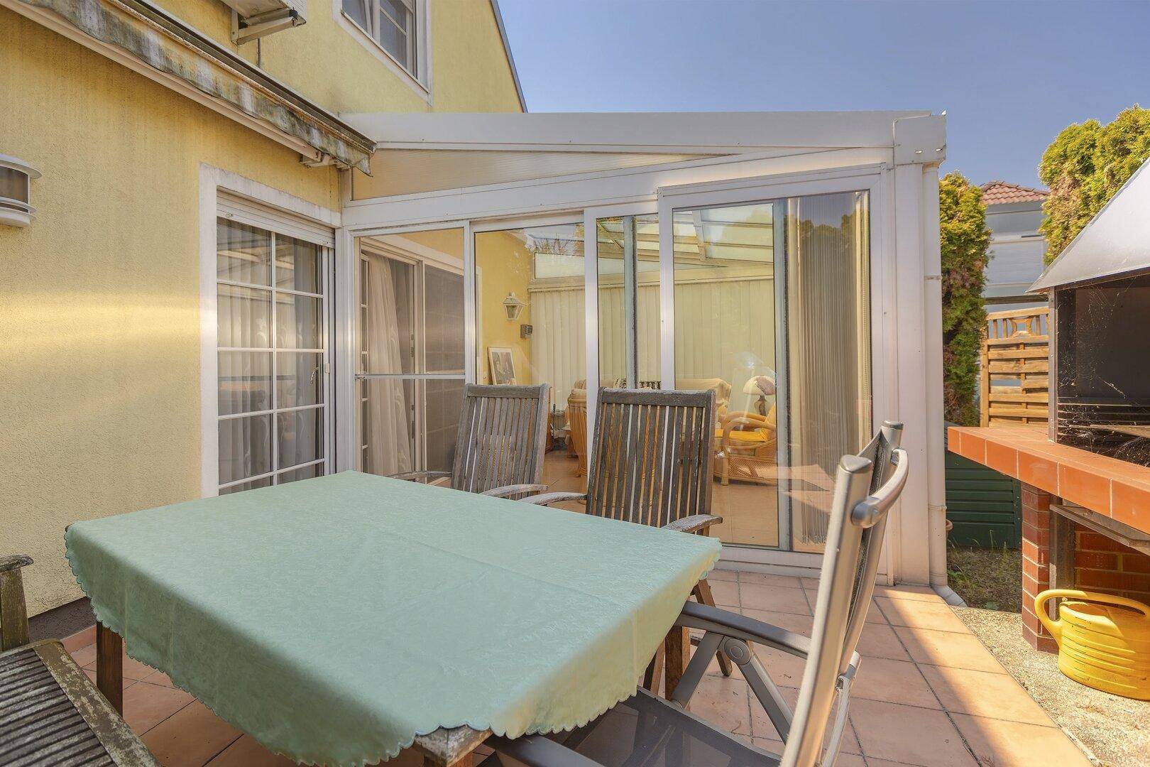 Terrasse mit Fliesenboden, Esstisch und gemauertem Grill, direkt am Wintergarten gelegen.