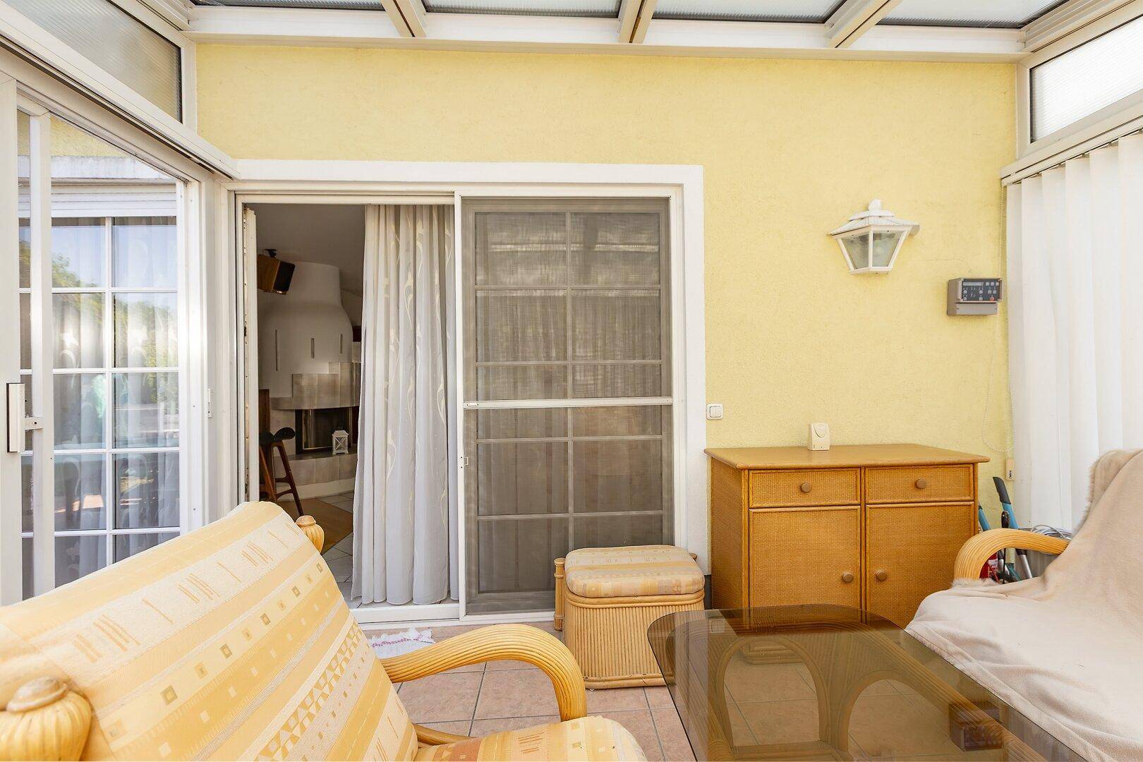 Gemütlicher Wintergarten mit Rattanmöbeln und Zugang zum Innenbereich des Hauses durch eine Schiebetür.
