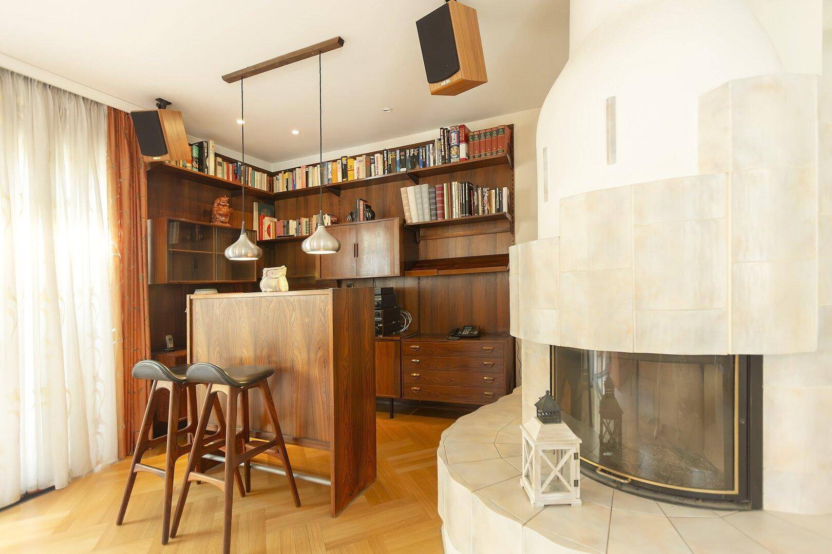 Wohnbereich mit Kamin, eingebauten Holzregalen und einer kleinen Bar mit Hockern und Parkettboden.