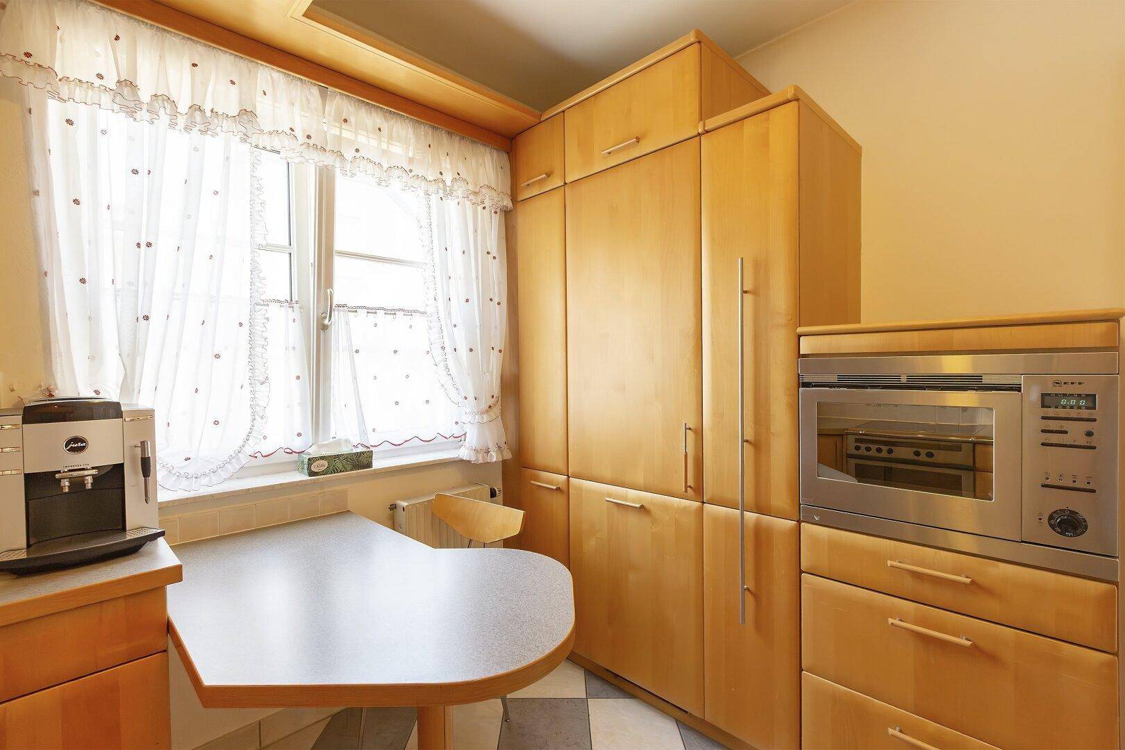 Helle Holzküche mit Fenster, integriertem Kühlschrank und Mikrowelle, mit viel Stauraum.