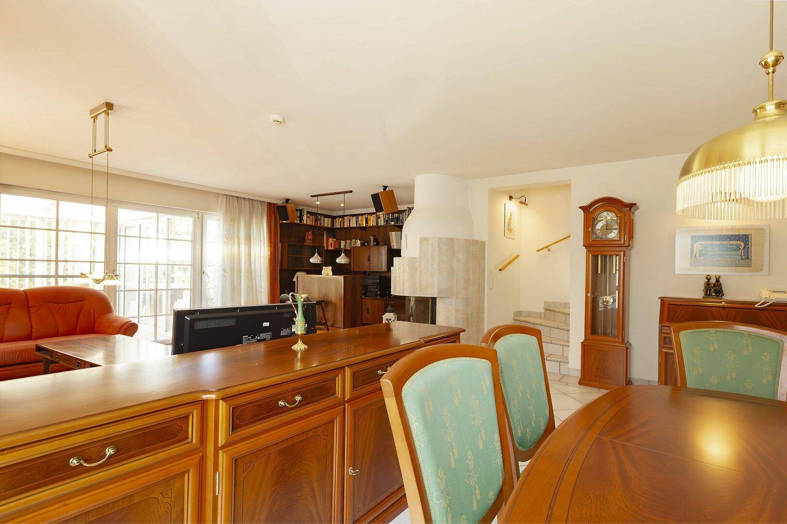 Offener Wohn-Essbereich mit Kamin, traditionellen Holzmöbeln und Treppenaufgang im Hintergrund.