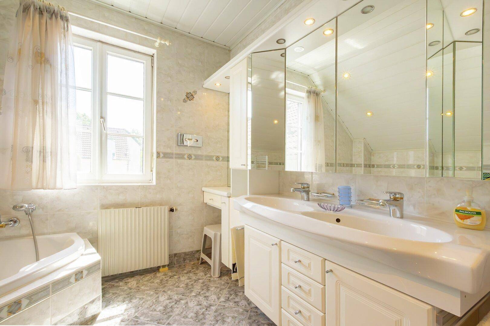 Helles Badezimmer mit Doppelwaschbecken, Spiegelschrank und Fenster.