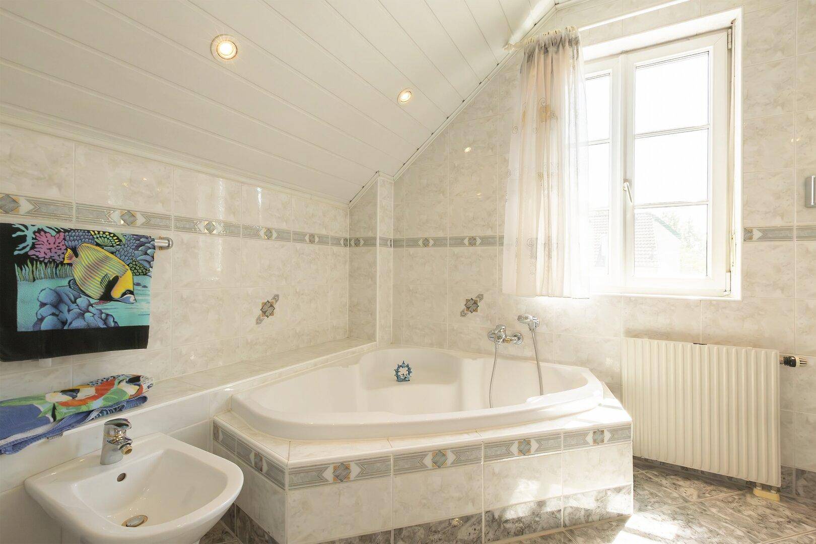 Badezimmer mit Eckbadewanne, Bidet und Fenster unter der Dachschräge.