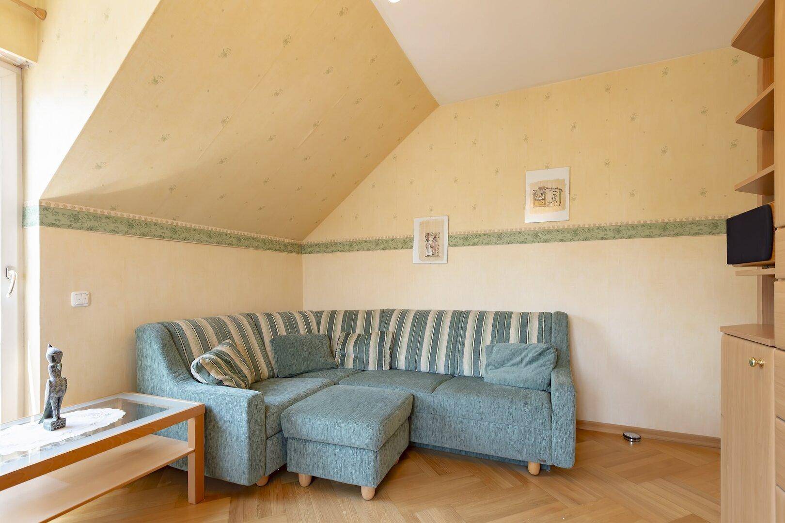 Gemütliches Schlafzimmer im Dachgeschoss mit schräger Decke, Sofa und Parkettboden, hell und einladend.