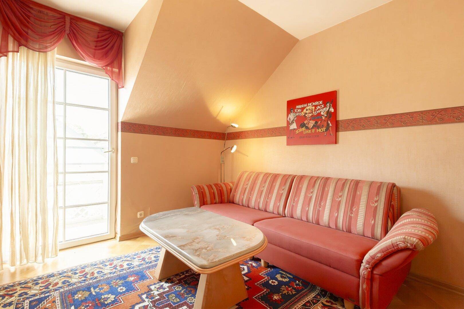Gemütliches Schlafzimmer im Dachgeschoss mit schräger Decke, Sofa und Zugang zum Balkon.