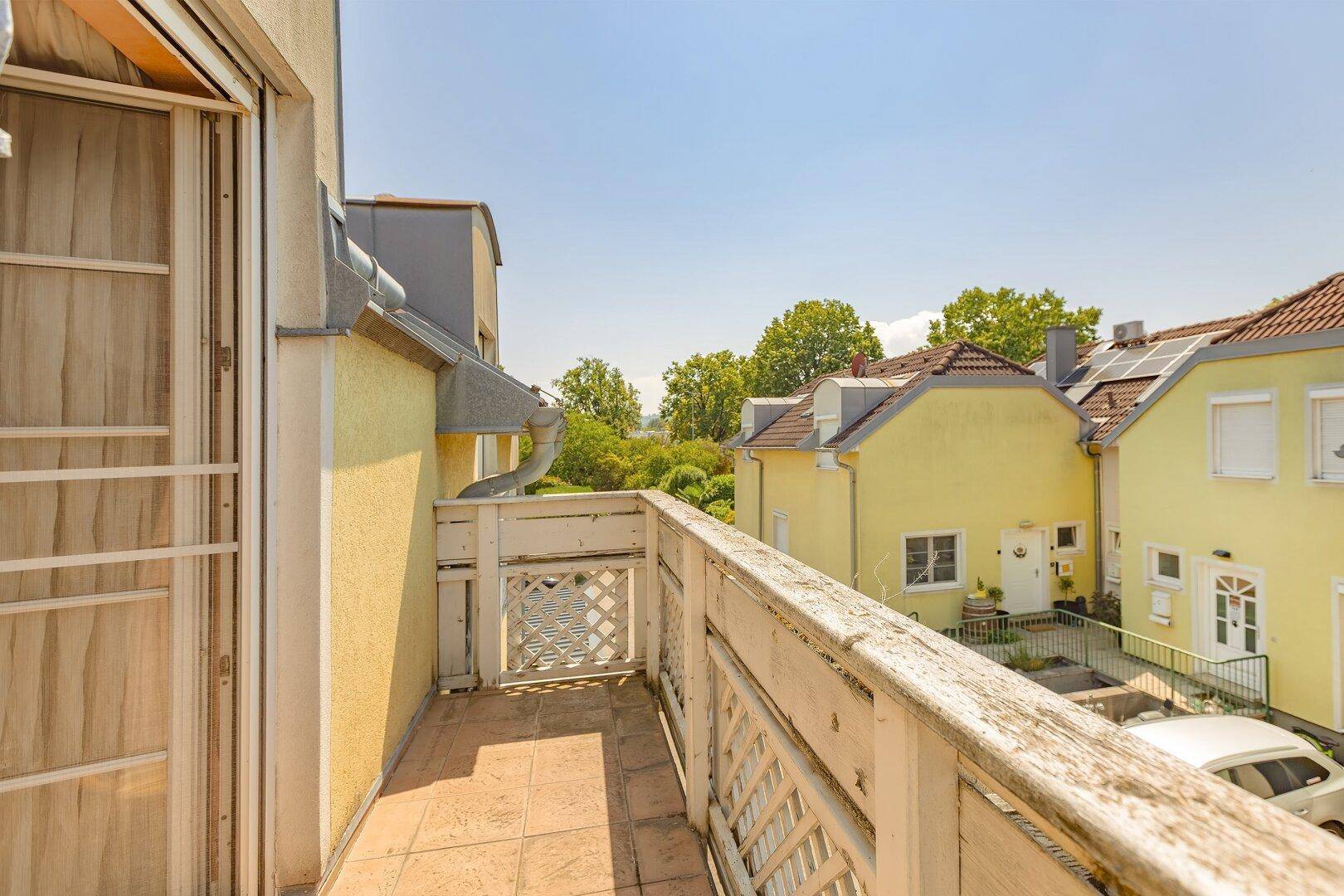 Balkon mit Fliesenboden und Holzgeländer, bietet einen weiten Blick auf die grüne Umgebung.
