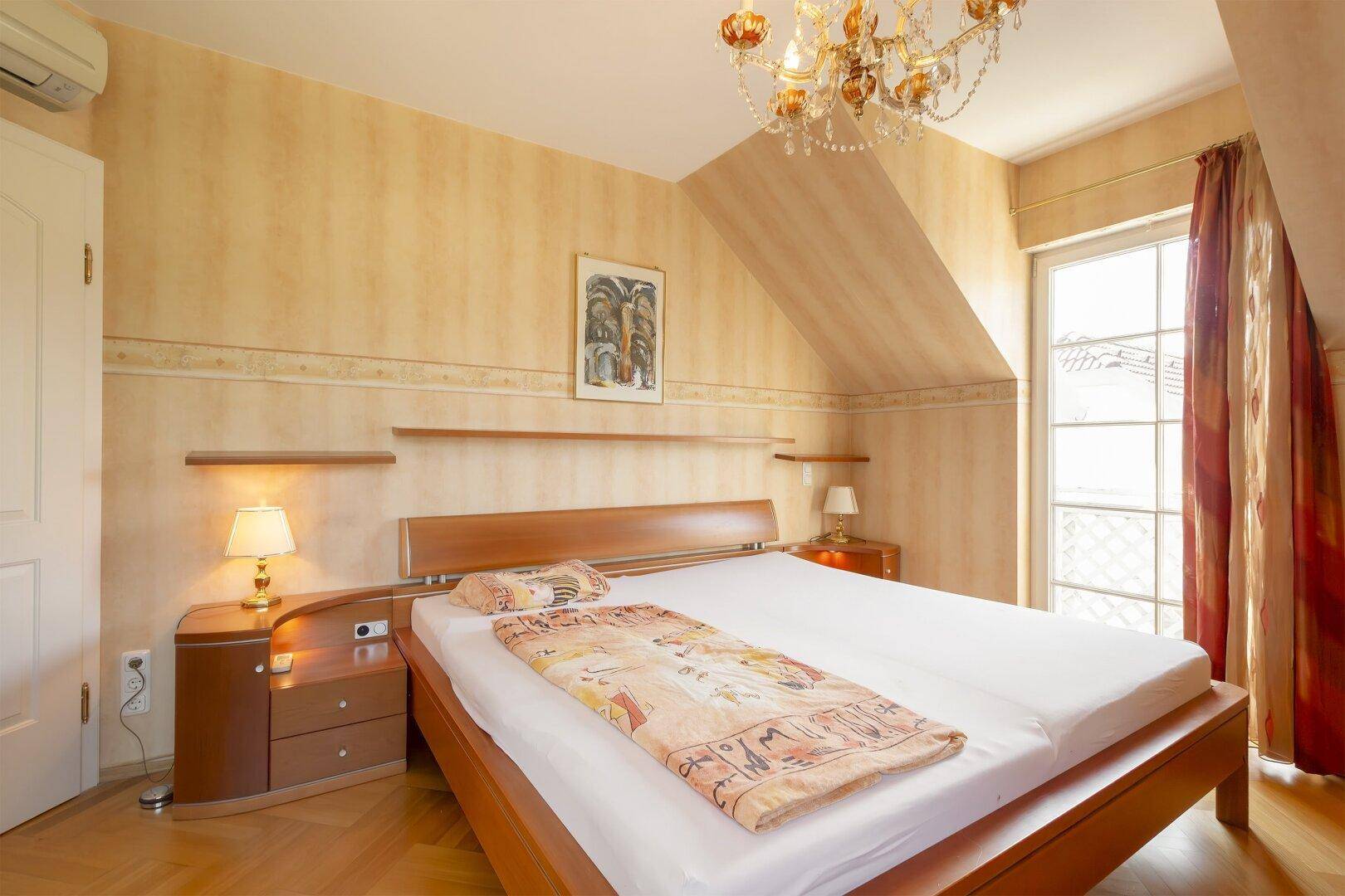 Helles Schlafzimmer mit Dachschräge, Doppelbett und Kronleuchter.