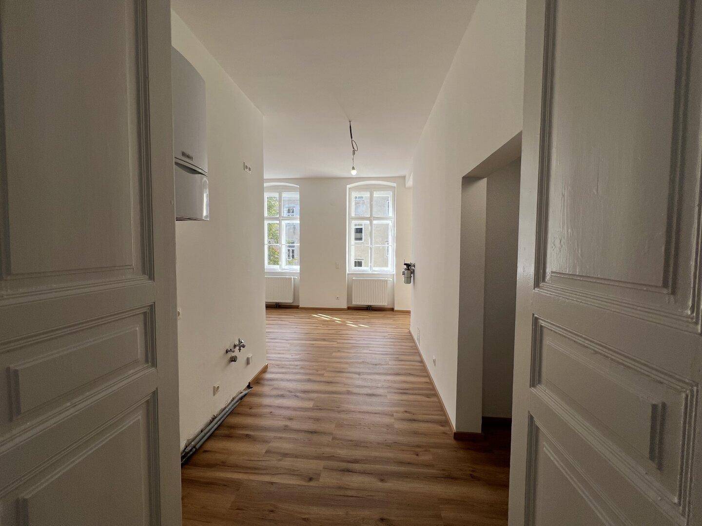 Großer, heller Raum mit Holzlaminatboden und sichtbaren Anschlüssen für eine zukünftige Küche.