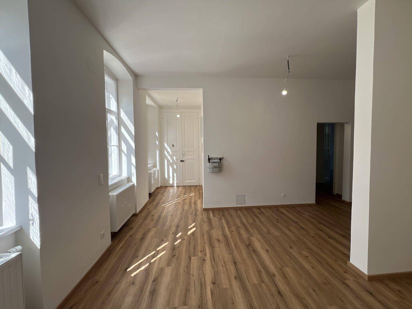 Lichtdurchfluteter Raum mit Holzlaminatboden und hohen Fenstern, die viel Tageslicht hereinlassen.