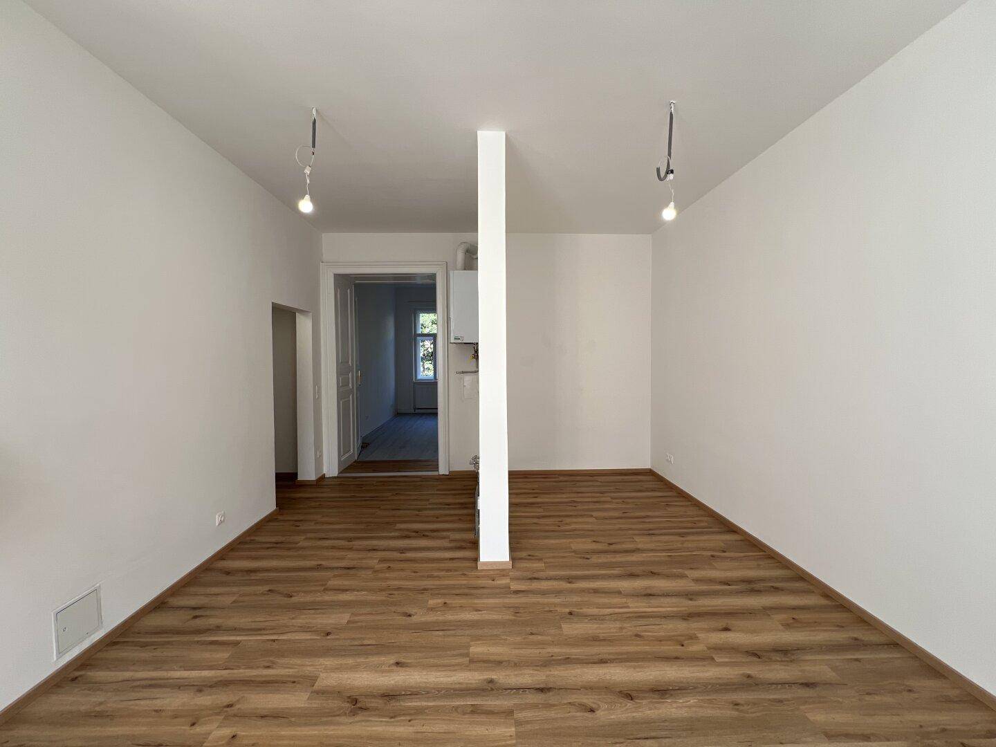 Langer, heller Raum mit Holzlaminatboden und einem Raumteiler, der zu weiteren Bereichen führt.