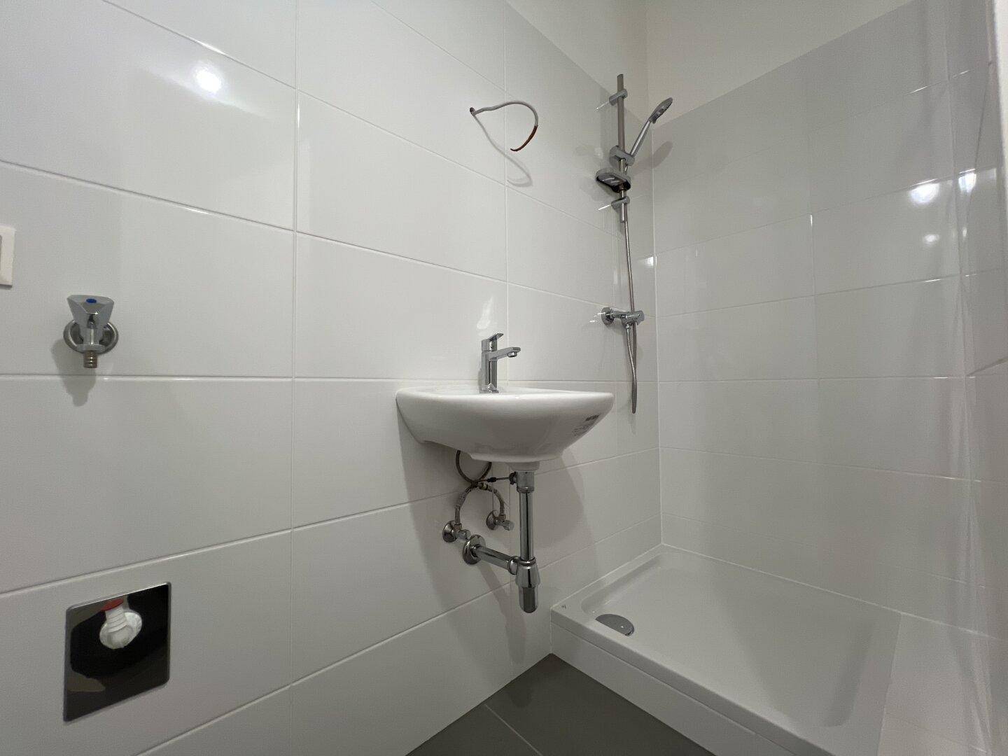 Modernes Badezimmer mit weißen Fliesen, Waschbecken und einer Duschkabine.