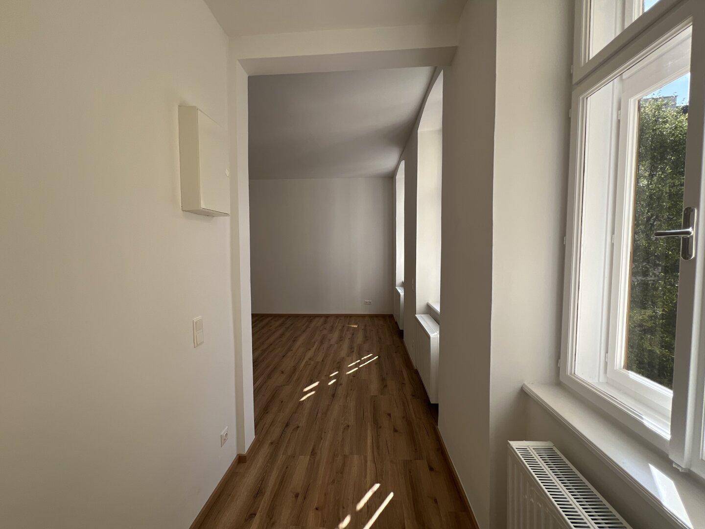 Heller Flur mit Holzlaminatboden und hohen Fenstern, die viel Licht in den Raum lassen.