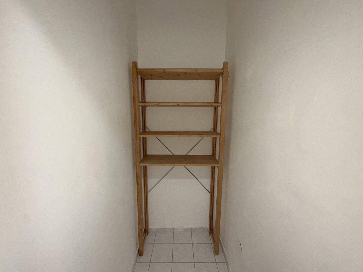 Kleine Nische mit Holzregal und gefliestem Boden, ideal als Abstellraum.