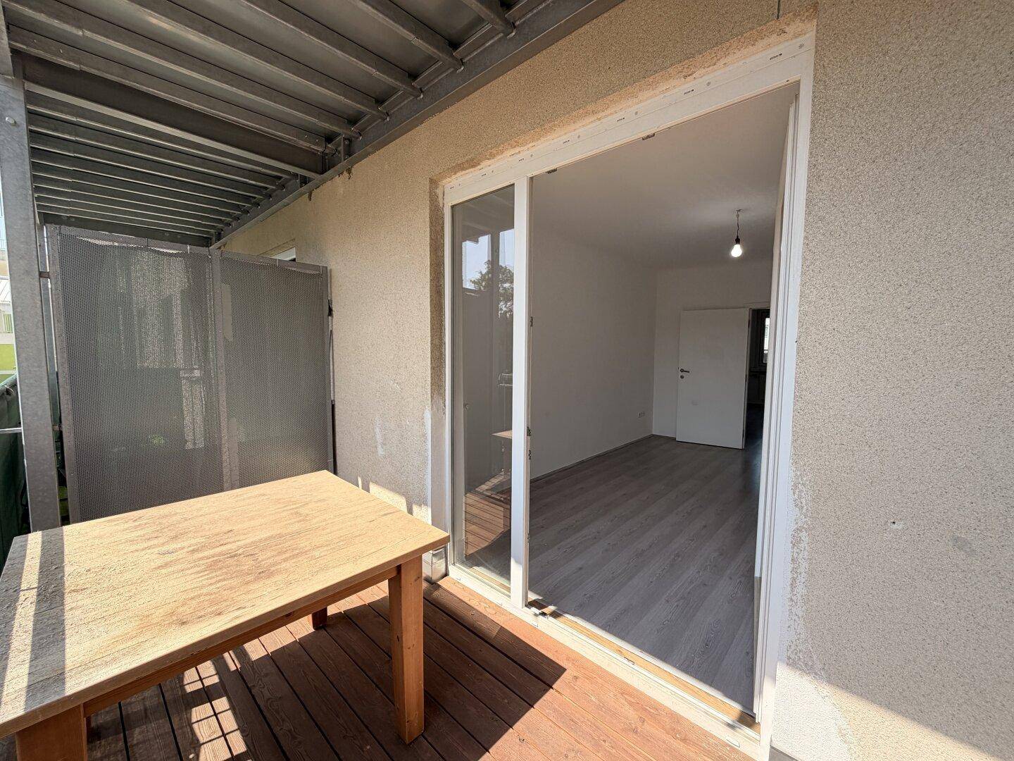 Balkon mit Holzboden und Schiebetür, die Zugang zu einem leeren Innenraum bietet.