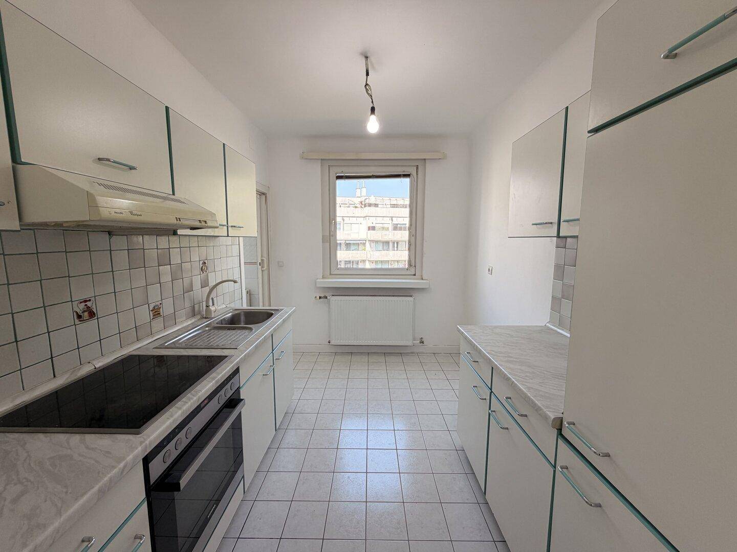 Helle Küche mit weißen Schränken, Fliesenboden und Fenster mit Stadtblick.