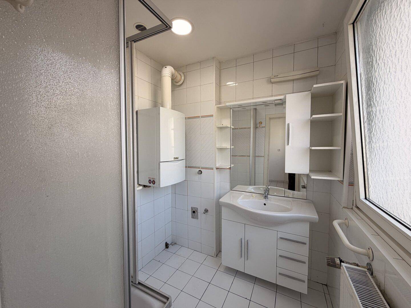 Gefliestes Badezimmer mit Duschkabine, Waschbecken, Fenster und Gastherme.