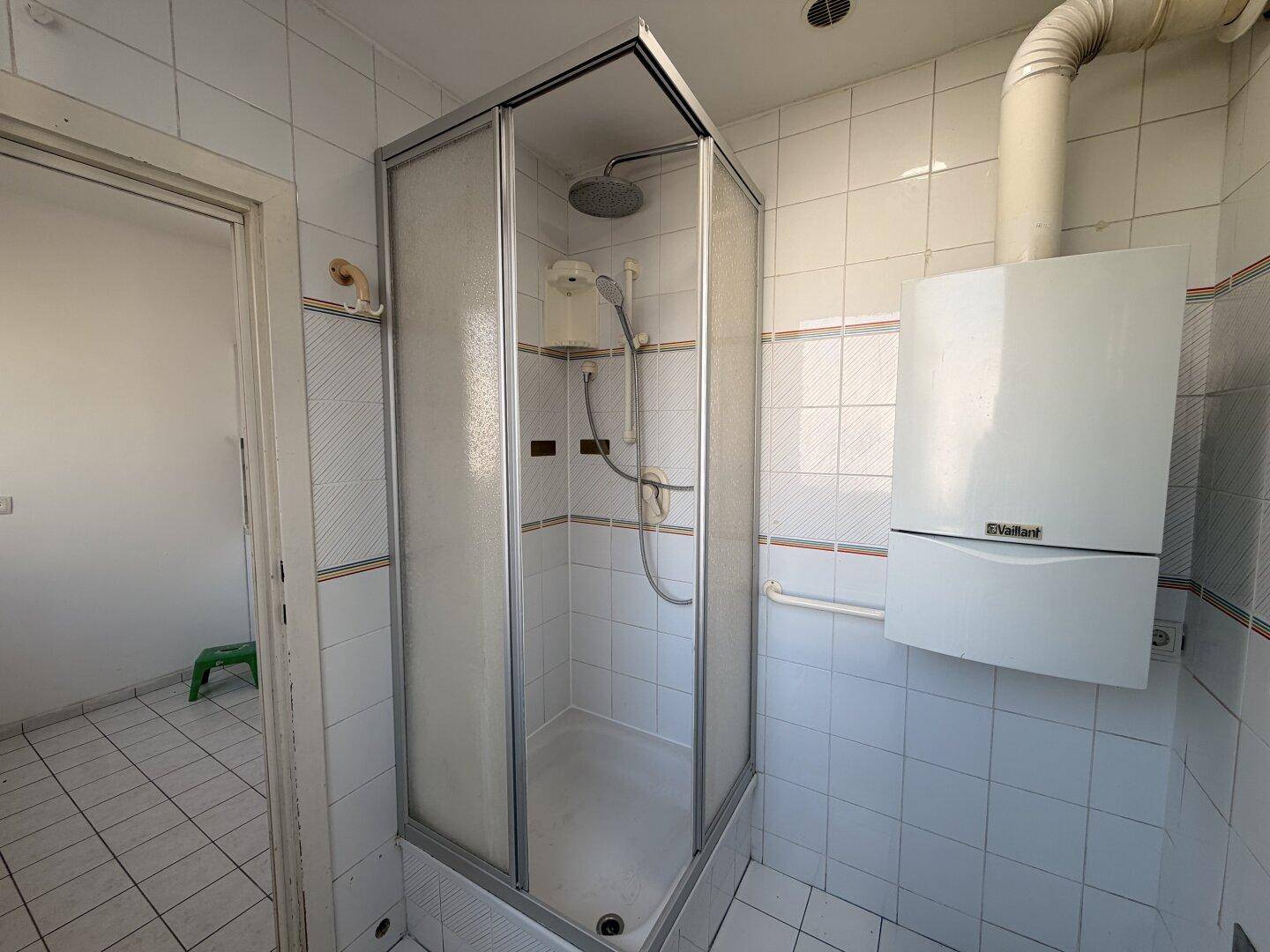 Badezimmer mit Duschkabine, weißen Fliesen und einer Gastherme an der Wand.