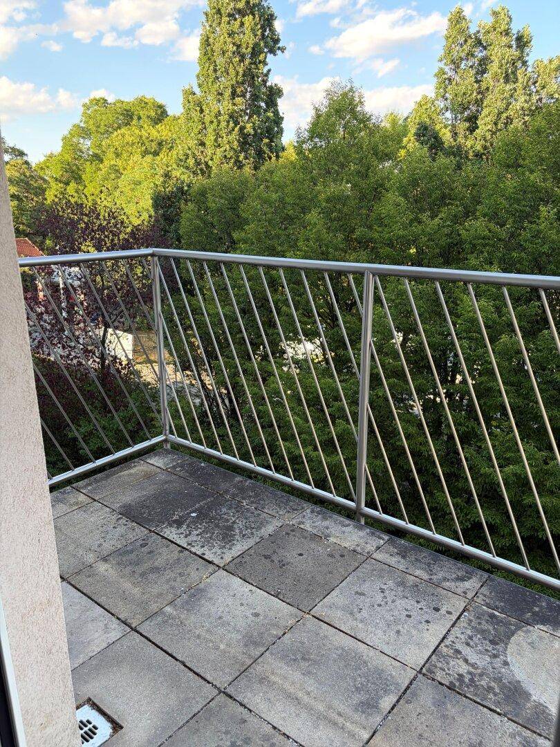 Geräumiger Balkon mit Fliesenboden und Blick auf hohe Bäume.