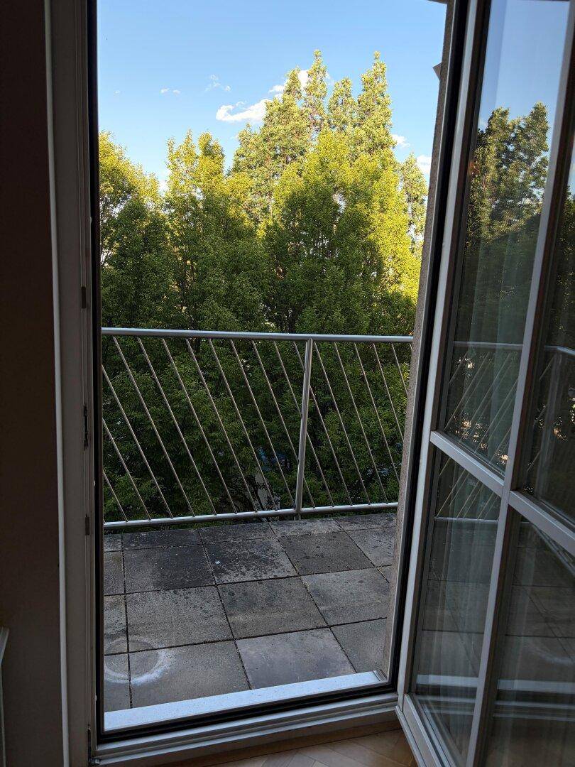 Blick aus einem Innenraum auf einen Balkon mit grüner Umgebung.