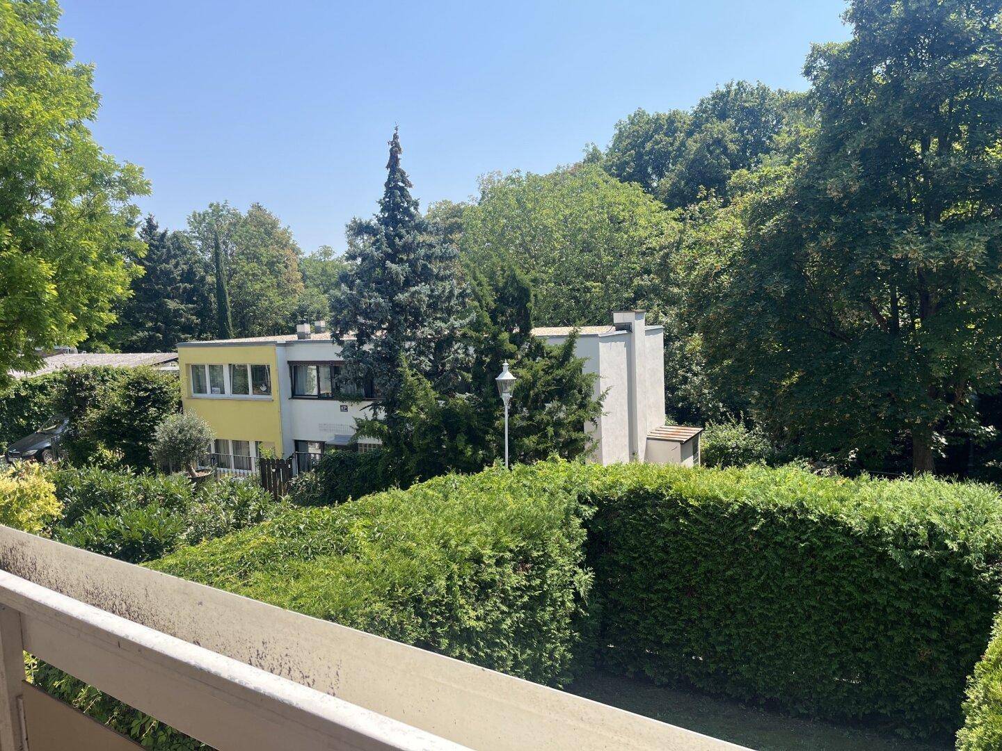 Blick von einem Balkon auf benachbarte Gebäude und eine grüne, bewaldete Umgebung.