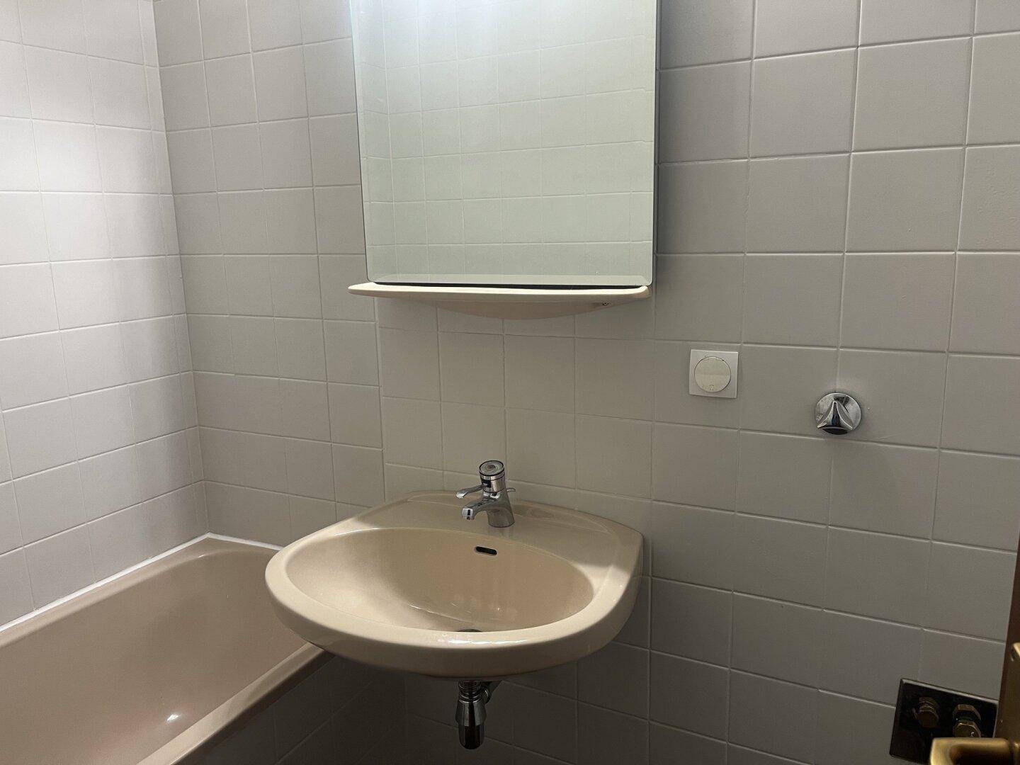 Badezimmer mit beigefarbener Badewanne, Waschbecken und weiß gefliesten Wänden.