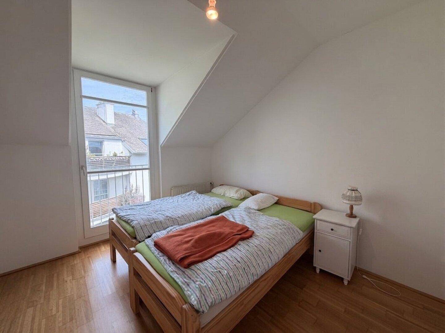 Schlafzimmer mit Holzboden, zwei Einzelbetten und einem Fenster mit Blick ins Grüne.