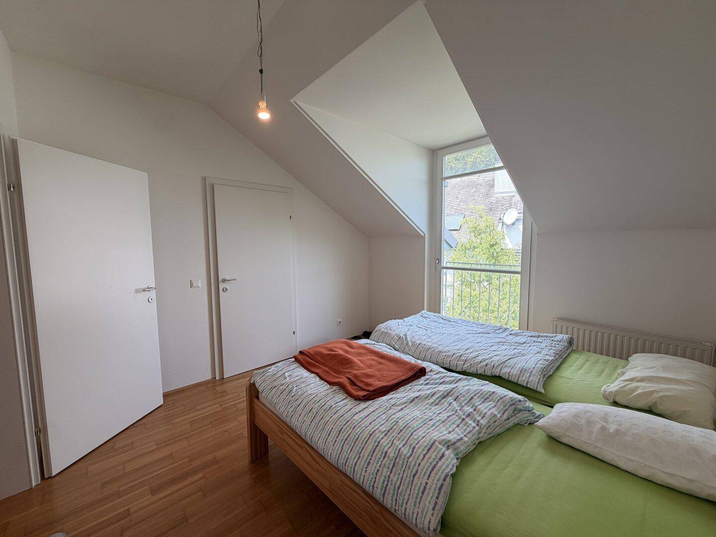 Helles Schlafzimmer mit Holzboden, Dachschräge und einem großen Fenster für viel Tageslicht.