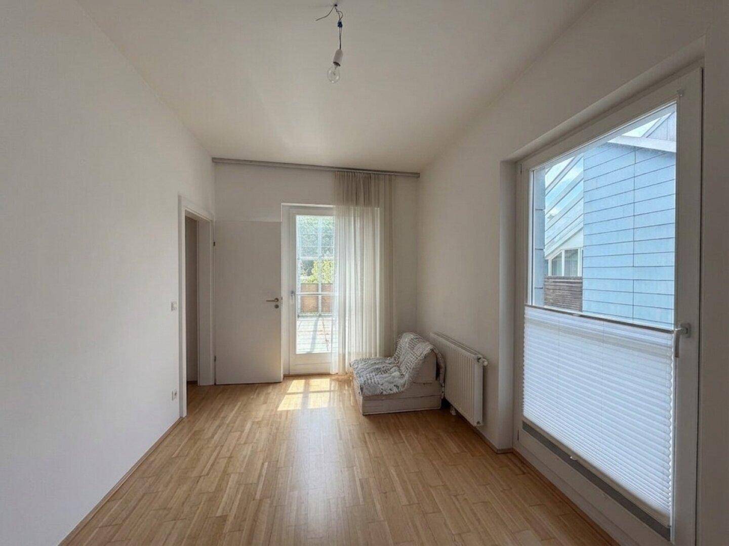 Heller Raum mit Holzboden, großen Fenstern und Zugang zu einem Außenbereich.