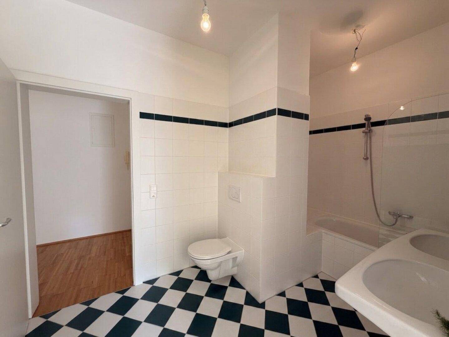 Badezimmer mit schwarz-weiß kariertem Fliesenboden, Badewanne und wandhängendem WC.