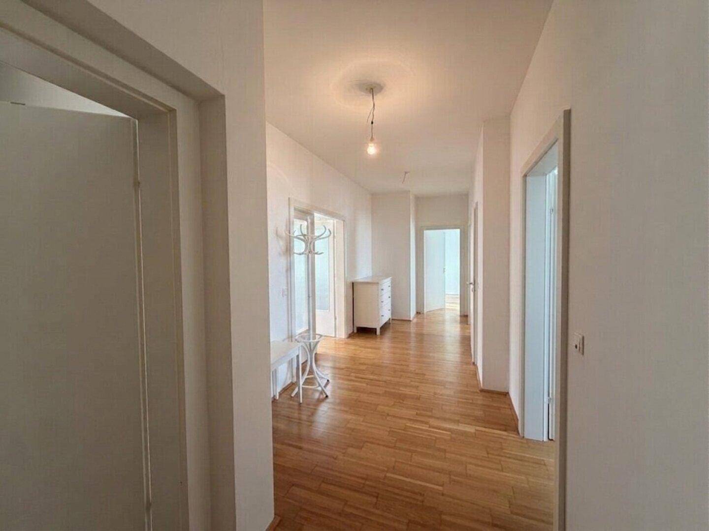 Heller Flur mit Holzboden, Garderobe und Zugang zu mehreren Zimmern.