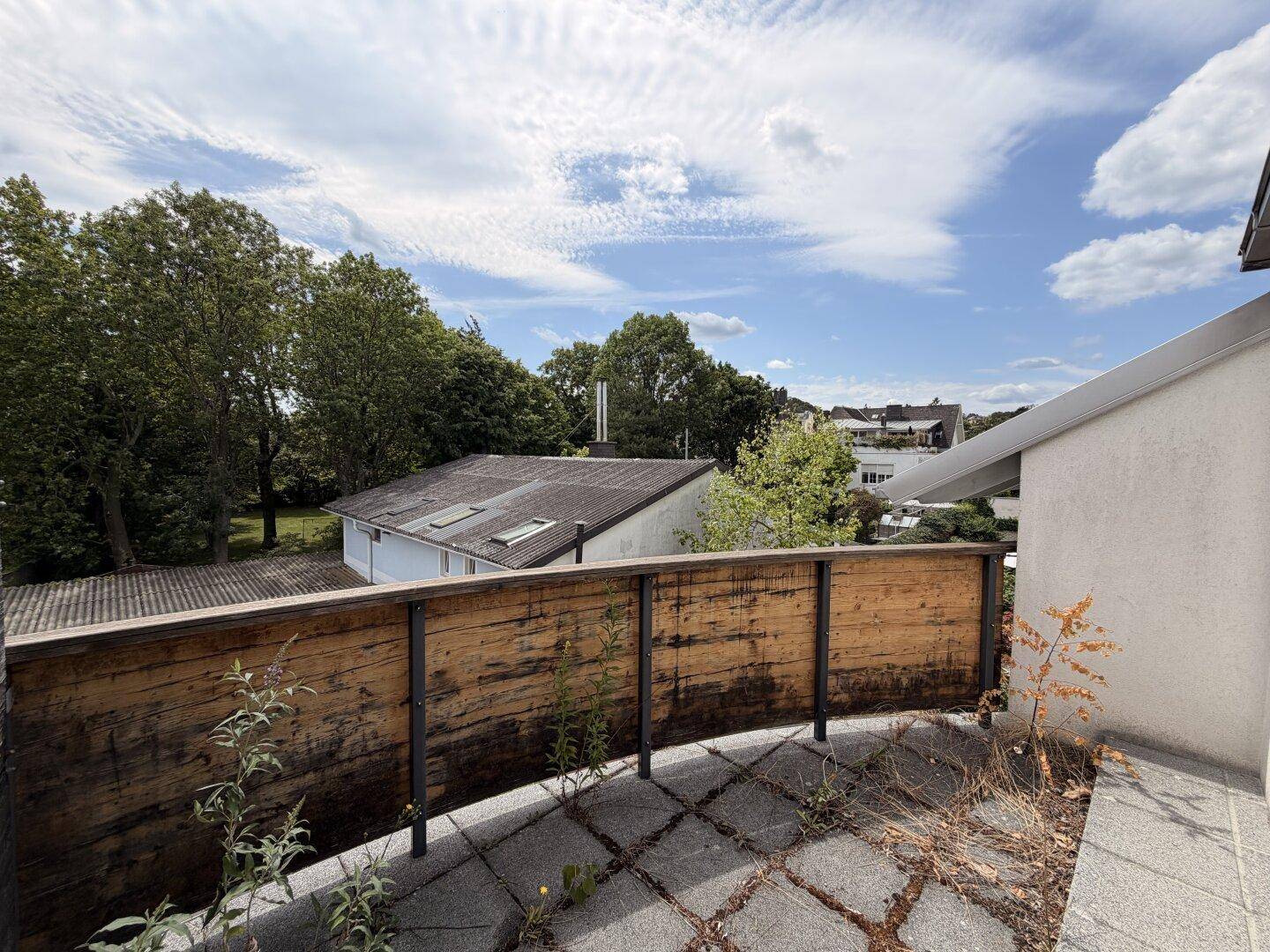 Balkon mit Holzzaun und Blick auf grüne Bäume und umliegende Dächer.