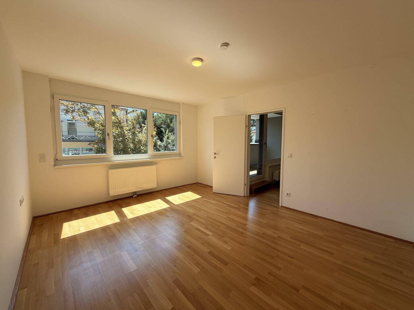 Helles Schlafzimmer mit Parkettboden und großen Fenstern, die viel Tageslicht hereinlassen.