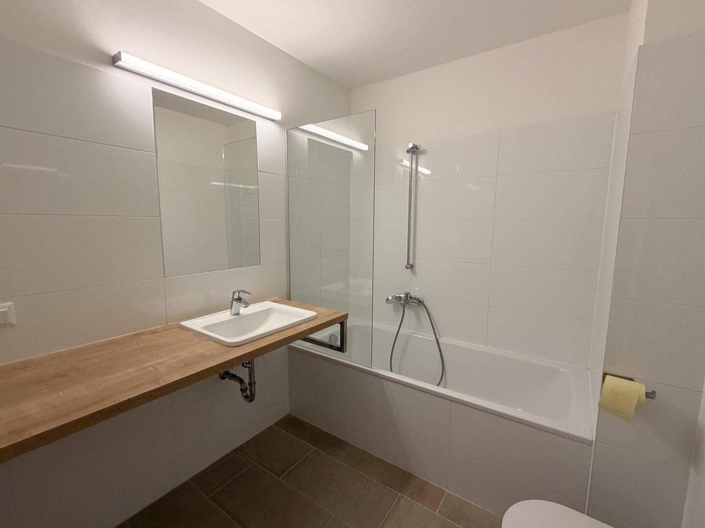 Modernes Badezimmer mit Badewanne, Duschwand, Einzelwaschbecken und Holzablage.