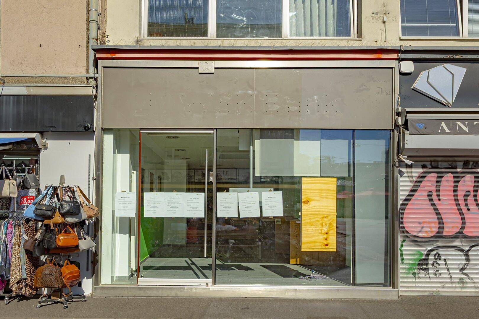 Ladenfront eines Geschäfts mit großen Schaufenstern, teilweise verdeckt, und Graffiti an der Seite.