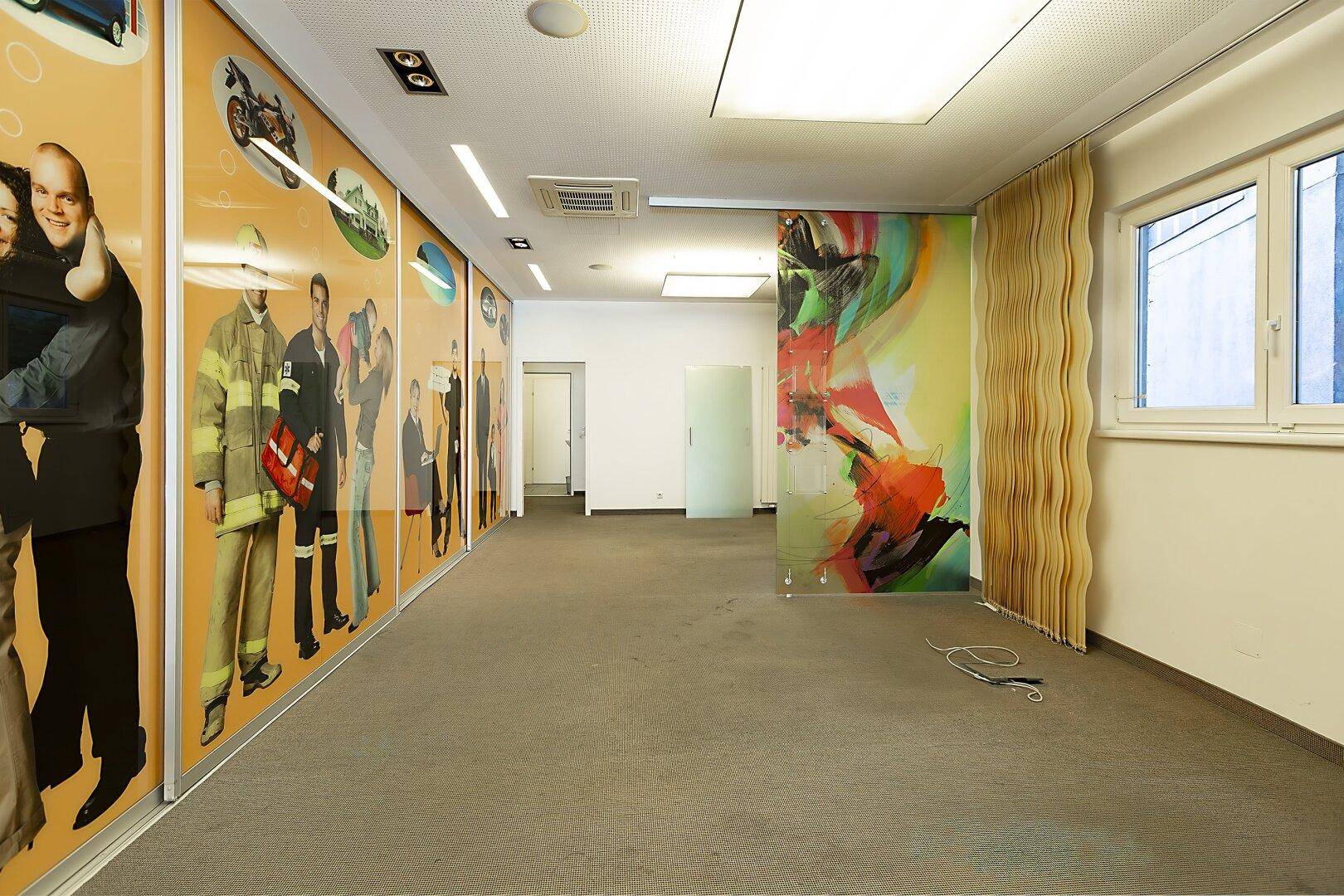 Geräumiger Flur in einem Geschäftsraum mit Teppichboden, farbiger Glastrennwand und großen Werbeflächen an der Wand.