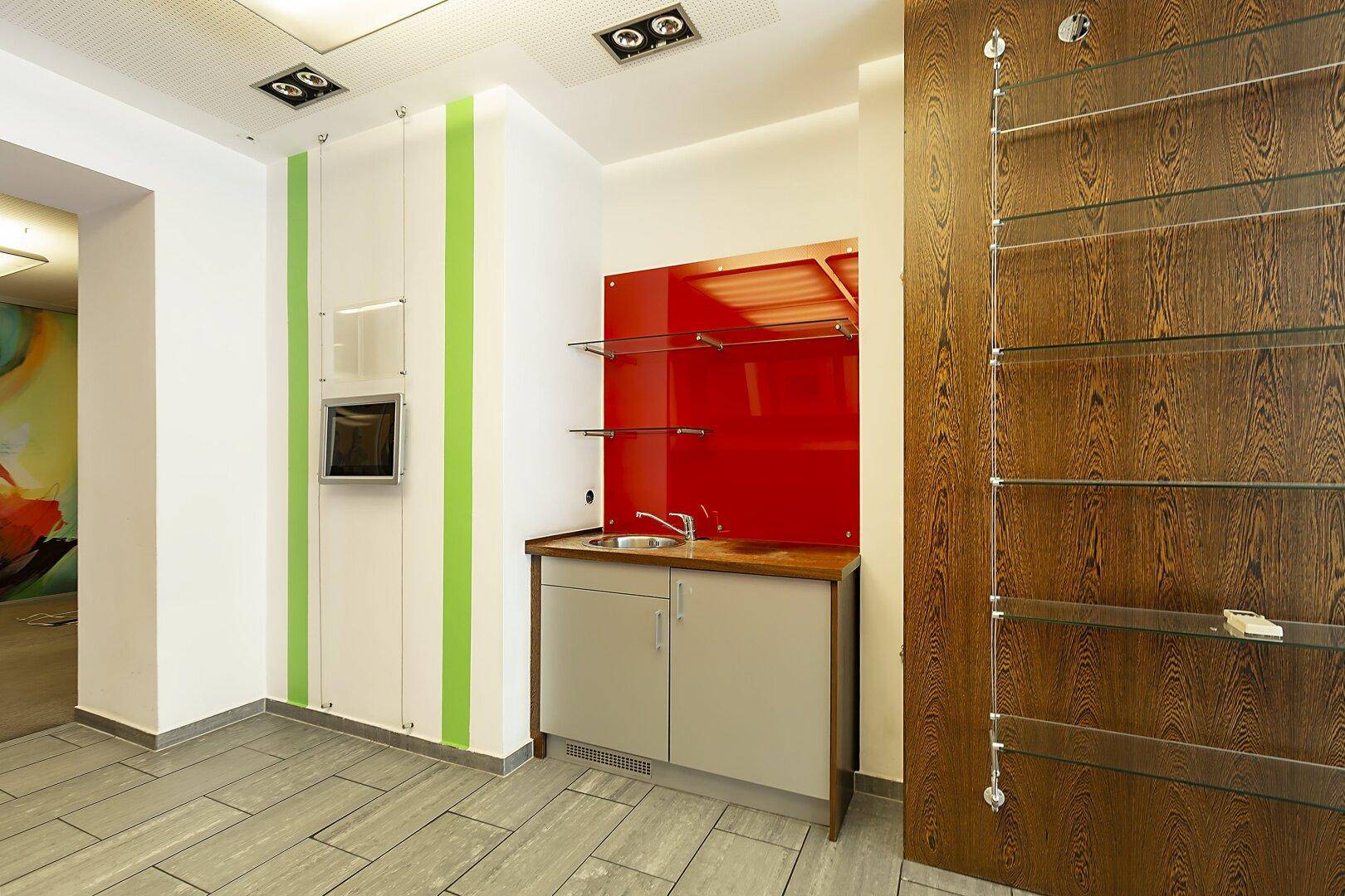 Kleine Küchenzeile oder Barbereich mit roter Rückwand, Spüle und integrierten Schränken in einem Geschäftsraum.