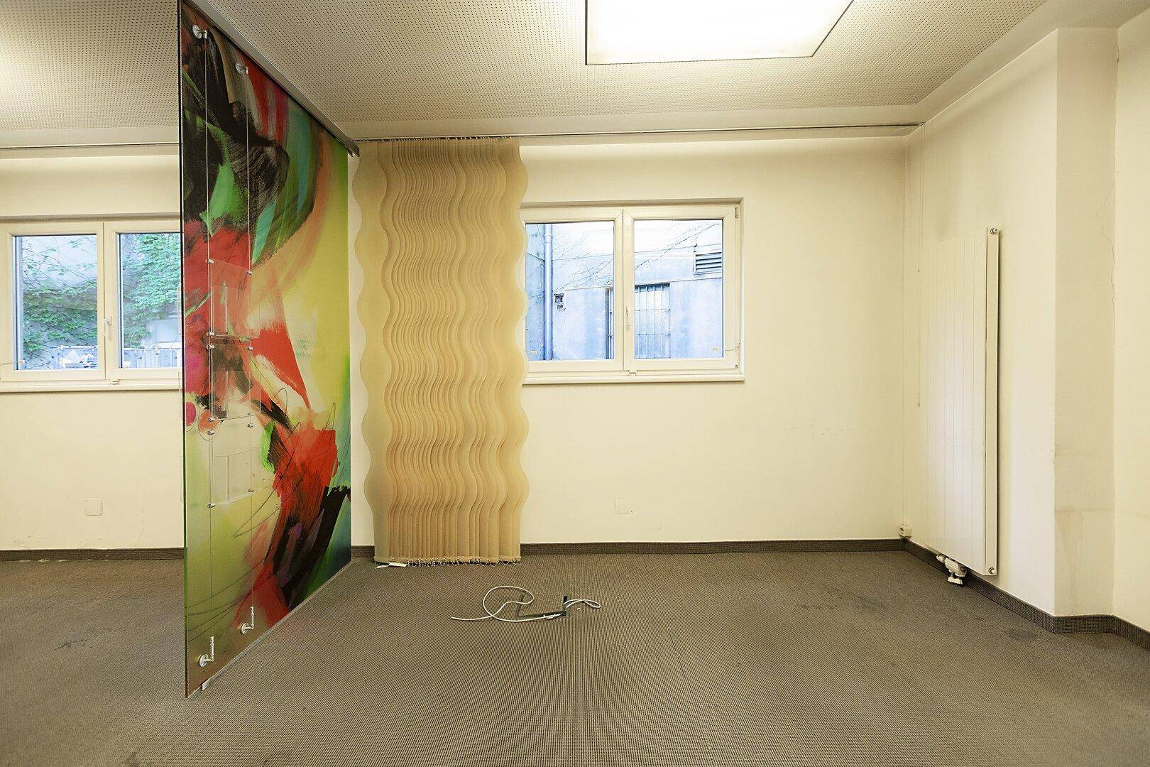 Büroraum mit Fenster, Teppichboden und einer farbenfrohen Glastrennwand als Gestaltungselement.
