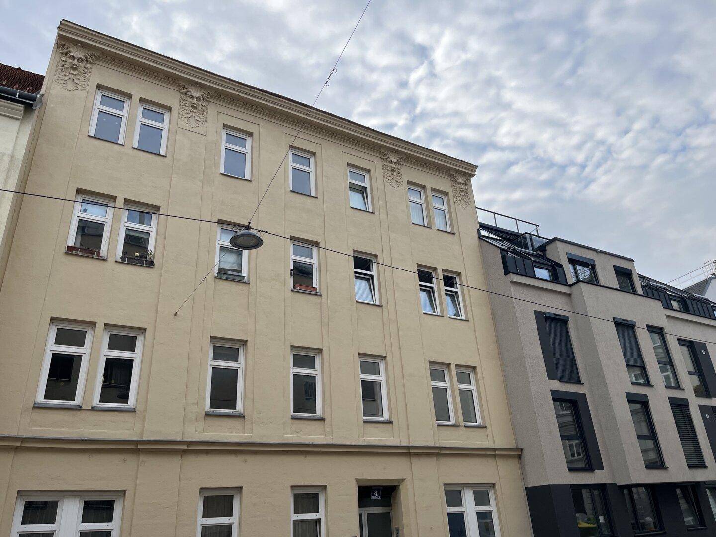 Gepflegte Altbaufassade mit dekorativen Verzierungen, angrenzend an ein modernes Gebäude mit Flachdach.