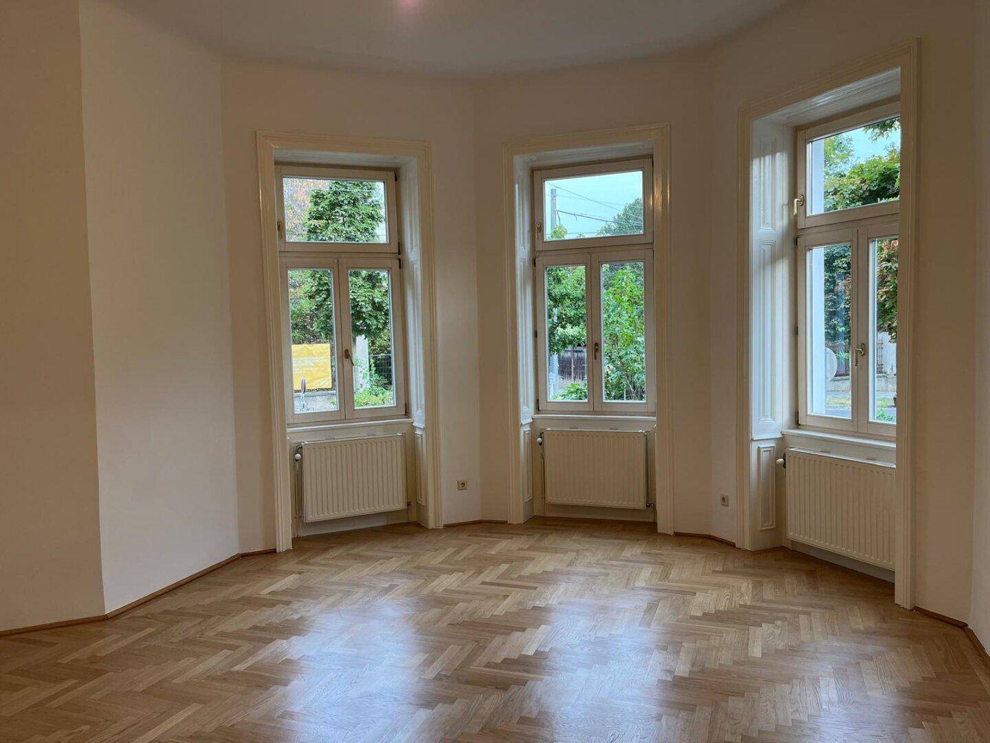 Geräumiges Wohnzimmer mit klassischem Fischgrätparkett und viel Tageslicht durch die Fenster.