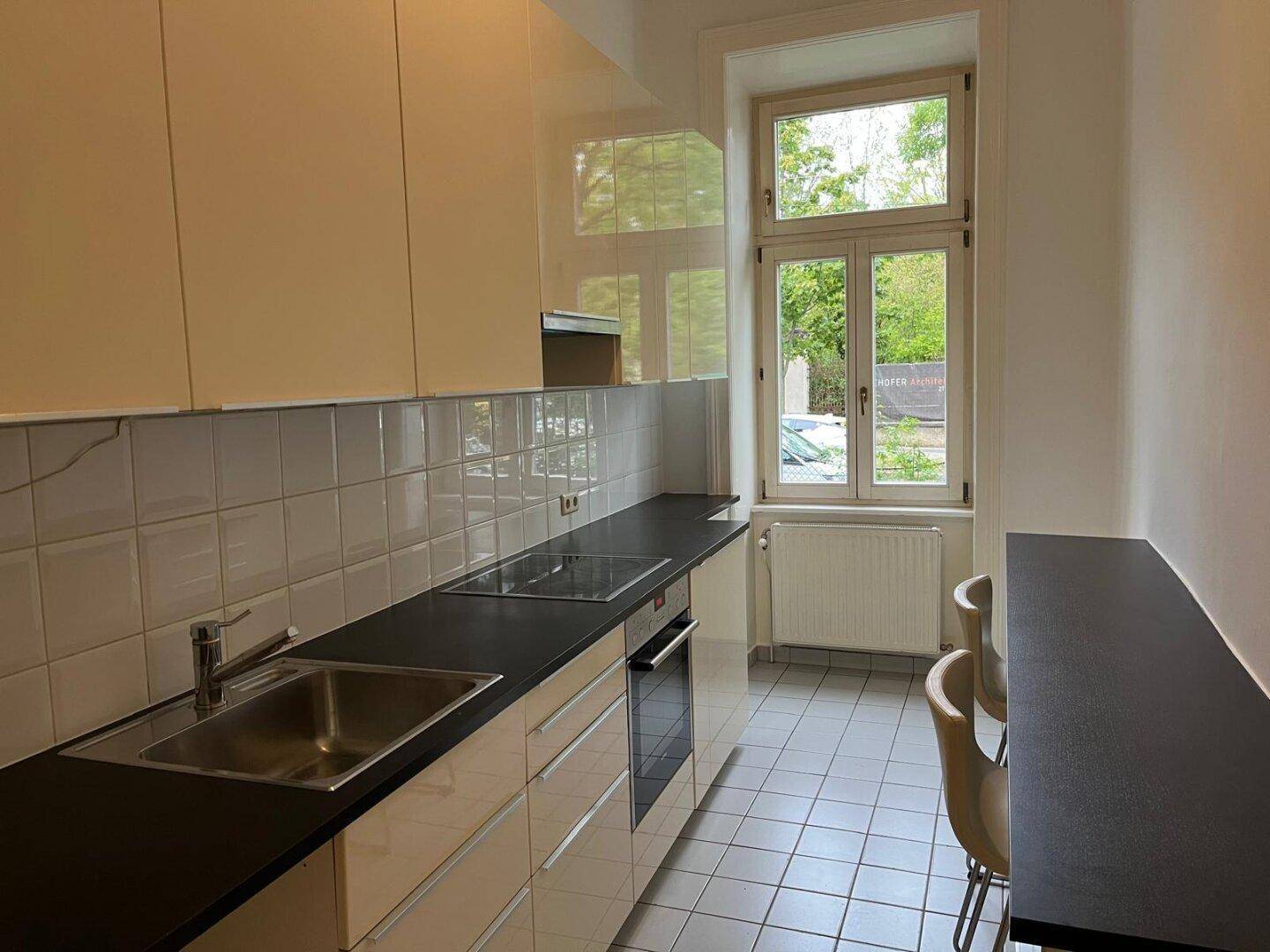 Moderne Küche mit beigen Hochglanzschränken, dunkler Arbeitsplatte und Fenster.