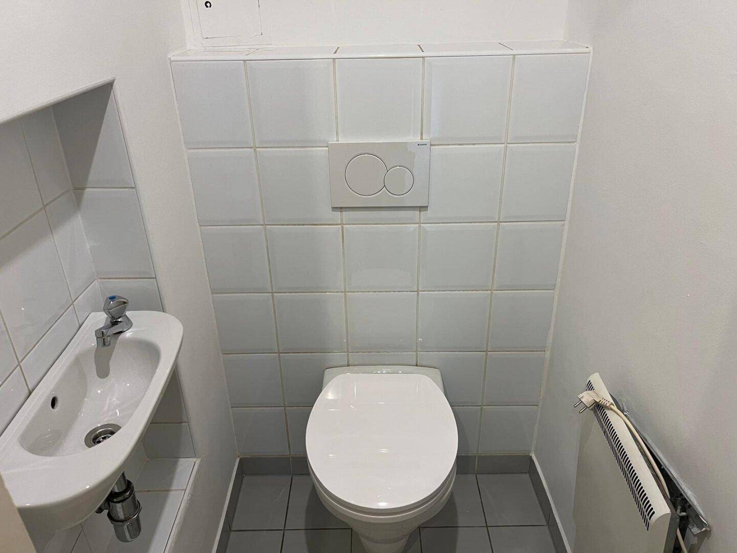 Kleines separates WC mit Wand-WC, Waschbecken und weißen Fliesen.