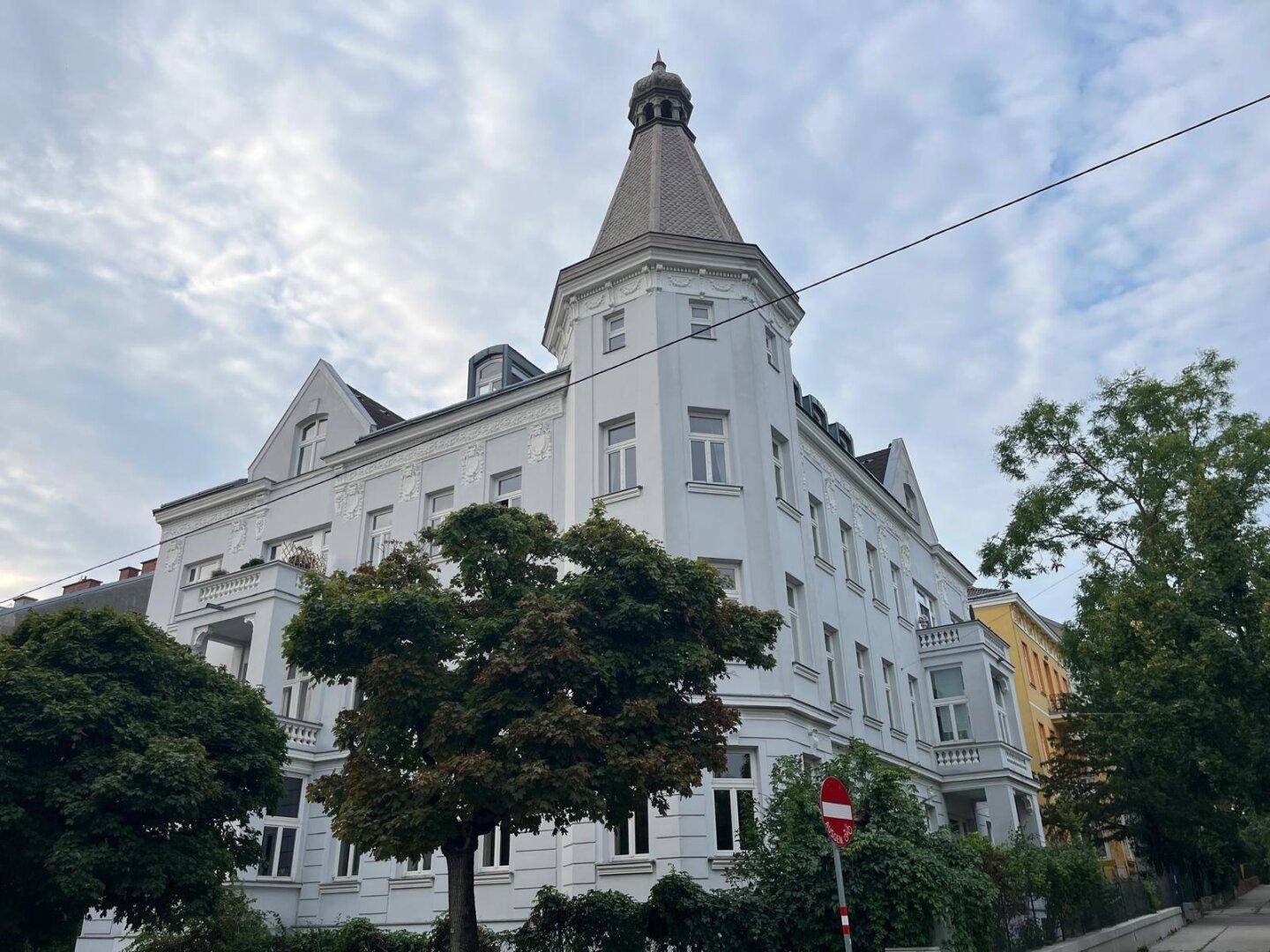 Elegantes Altbaugebäude mit markantem Turm und vielen Fenstern unter bewölktem Himmel.