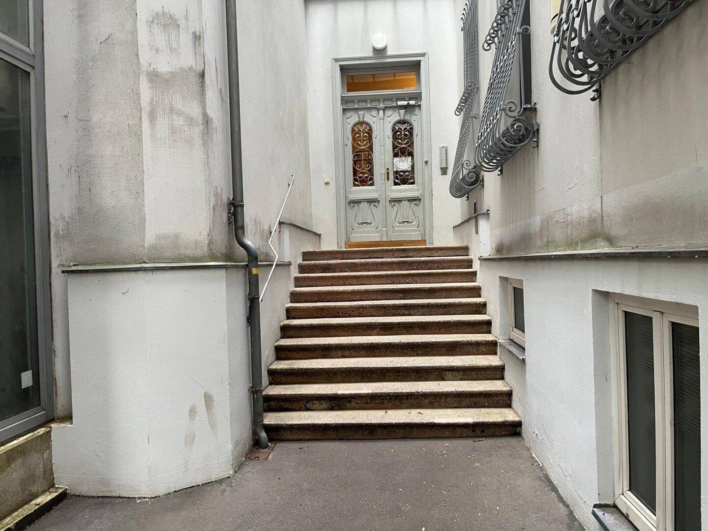 Eingangsbereich des Gebäudes mit Steintreppe und verzierter Holztür.