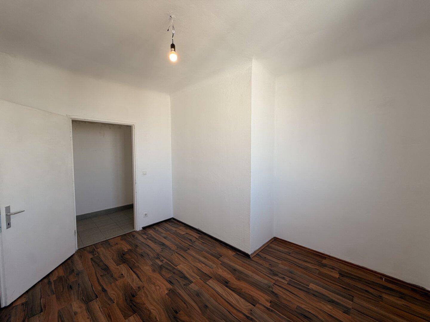 Leeres Zimmer mit dunklem Laminatboden und weiß gestrichenen Wänden, bereit zur individuellen Gestaltung.